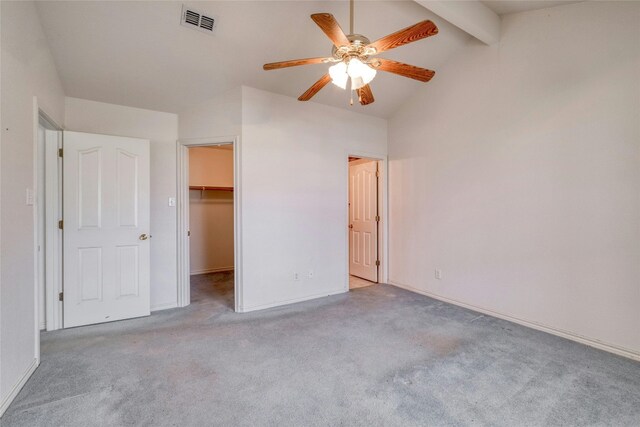 unfurnished bedroom with a closet, light colored carpet, vaulted ceiling with beams, a walk in closet, and ceiling fan