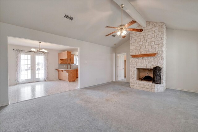 unfurnished living room with ceiling fan with notable chandelier, light colored carpet, vaulted ceiling with beams, a stone fireplace, and french doors