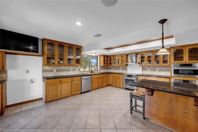 kitchen with tasteful backsplash, hanging light fixtures, wall chimney exhaust hood, appliances with stainless steel finishes, and dark stone countertops