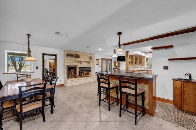 kitchen featuring a stone fireplace, a breakfast bar area, hanging light fixtures, and sink