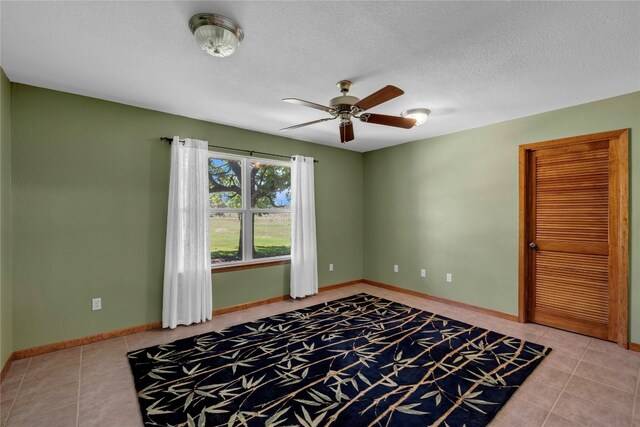 tiled empty room with ceiling fan and a textured ceiling