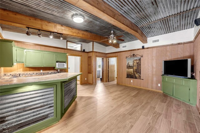 interior space featuring ceiling fan, beamed ceiling, wood walls, light hardwood / wood-style flooring, and green cabinets