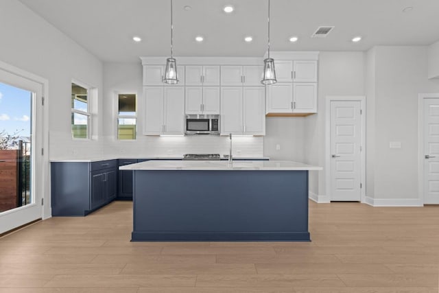 kitchen featuring white cabinetry, tasteful backsplash, an island with sink, blue cabinets, and decorative light fixtures