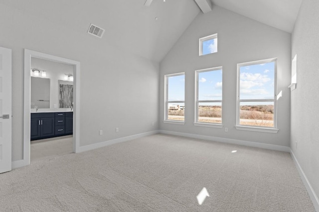 unfurnished bedroom featuring ensuite bath, beam ceiling, high vaulted ceiling, and light carpet