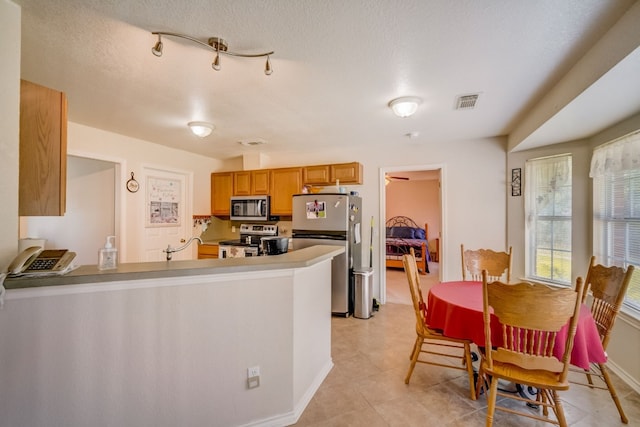 kitchen featuring kitchen peninsula, a textured ceiling, appliances with stainless steel finishes, and light tile patterned floors