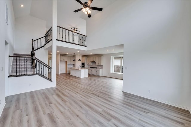 unfurnished living room with light hardwood / wood-style flooring, high vaulted ceiling, ceiling fan, and sink