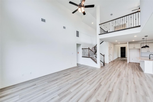 unfurnished living room with a towering ceiling, light hardwood / wood-style flooring, and ceiling fan