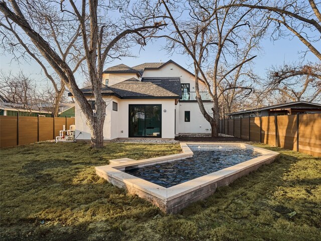 rear view of property featuring roof with shingles, a lawn, a fenced backyard, and stucco siding