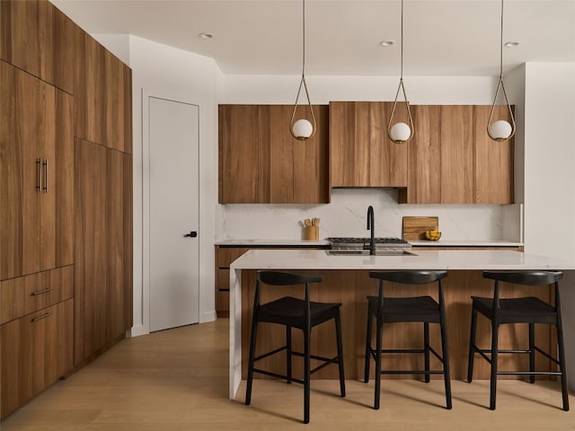 kitchen featuring a breakfast bar, light wood finished floors, tasteful backsplash, a sink, and modern cabinets