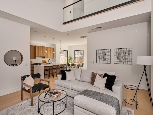 living area with light wood-style floors, baseboards, a high ceiling, and visible vents