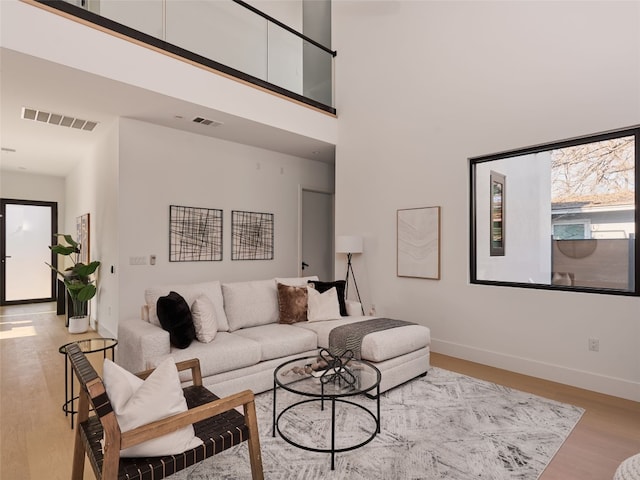 living area featuring visible vents, a towering ceiling, baseboards, and wood finished floors