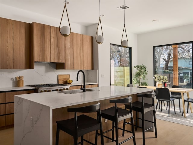 kitchen featuring an island with sink, modern cabinets, brown cabinets, a sink, and backsplash