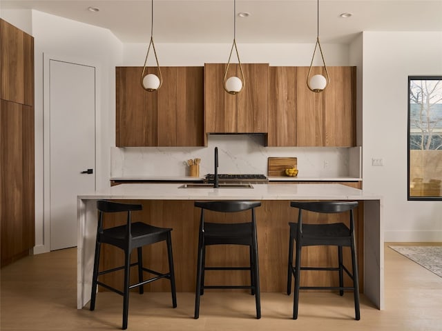 kitchen featuring tasteful backsplash, modern cabinets, brown cabinetry, and a sink