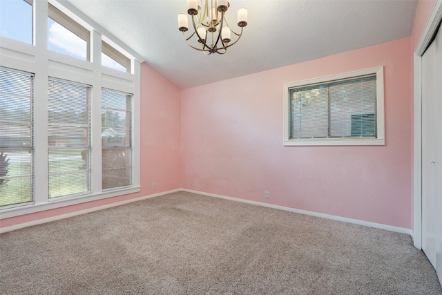 carpeted spare room with an inviting chandelier and vaulted ceiling