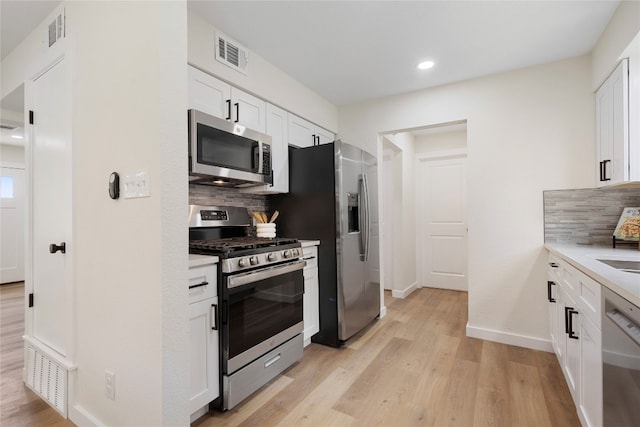 kitchen with appliances with stainless steel finishes, backsplash, light hardwood / wood-style flooring, and white cabinets