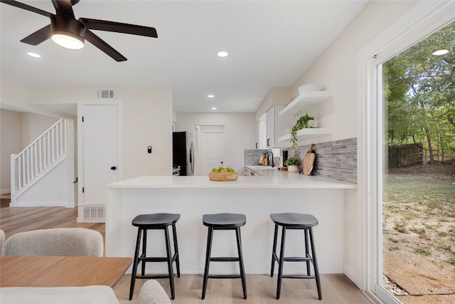 kitchen with white cabinets, kitchen peninsula, tasteful backsplash, and stainless steel refrigerator