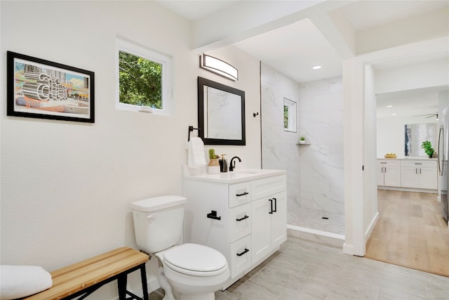 bathroom featuring ceiling fan, vanity, toilet, a tile shower, and hardwood / wood-style floors