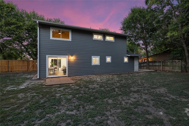 back house at dusk featuring a lawn