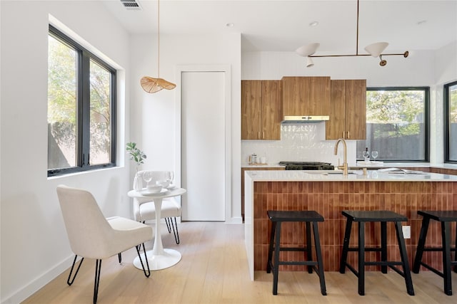 kitchen with a kitchen bar, light wood-type flooring, ventilation hood, and hanging light fixtures