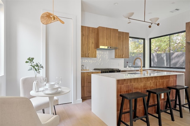 kitchen featuring backsplash, extractor fan, pendant lighting, light hardwood / wood-style floors, and a breakfast bar area