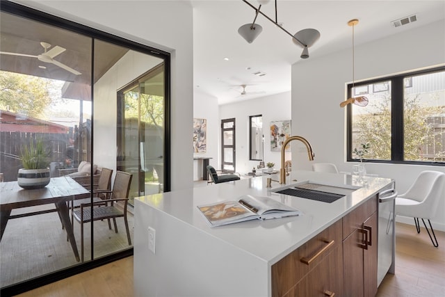 kitchen featuring sink, hanging light fixtures, ceiling fan, light wood-type flooring, and an island with sink