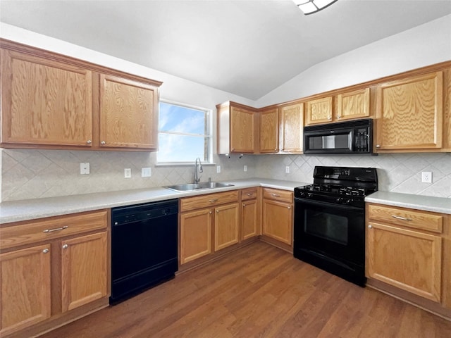 kitchen featuring sink, wood-type flooring, black appliances, vaulted ceiling, and decorative backsplash