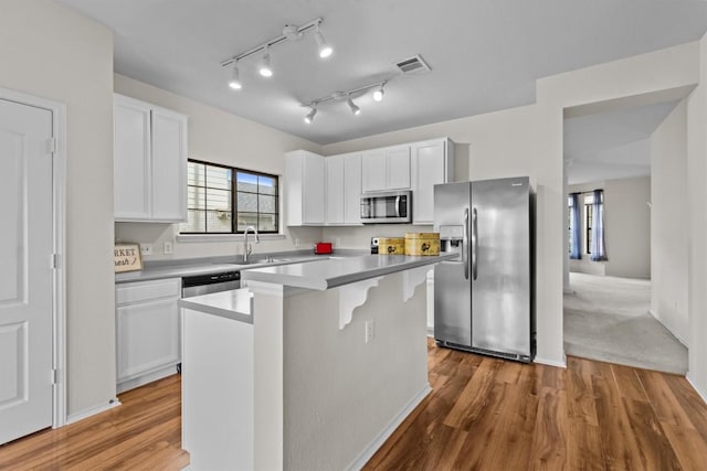 kitchen with appliances with stainless steel finishes, white cabinetry, a kitchen island, and hardwood / wood-style floors