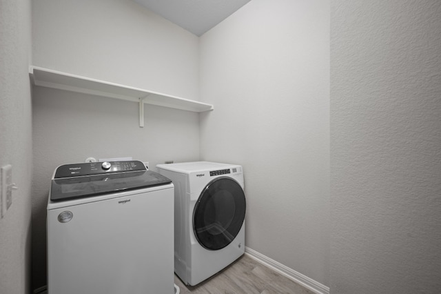 clothes washing area with washing machine and dryer and light hardwood / wood-style flooring