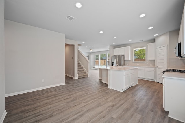 kitchen with an island with sink, stainless steel appliances, light hardwood / wood-style floors, decorative backsplash, and white cabinets