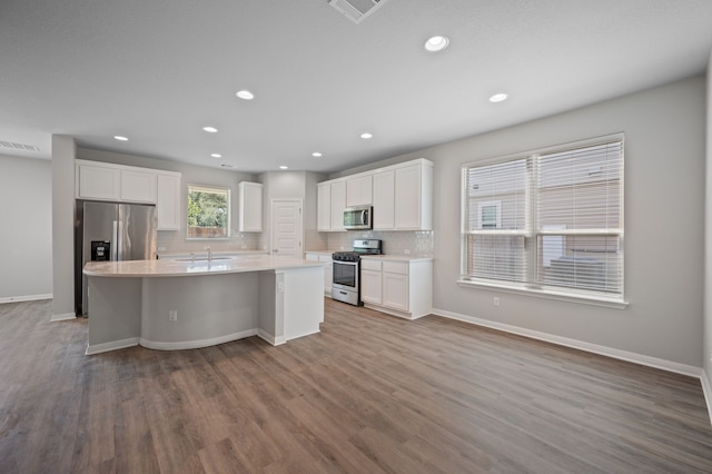 kitchen with stainless steel appliances, white cabinetry, light hardwood / wood-style floors, an island with sink, and backsplash