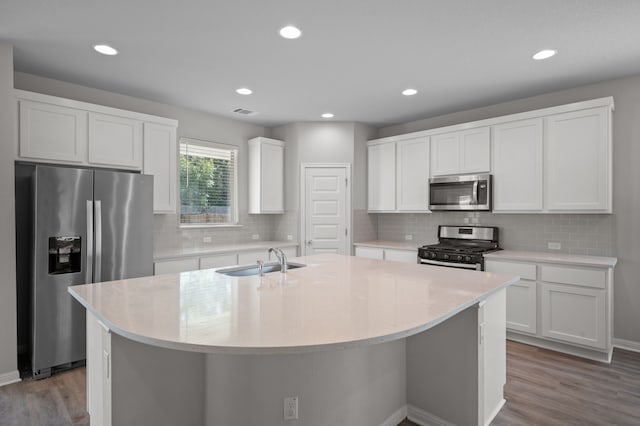 kitchen with stainless steel appliances, white cabinets, sink, and an island with sink