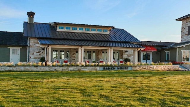 rear view of house with metal roof, a yard, a standing seam roof, and stone siding