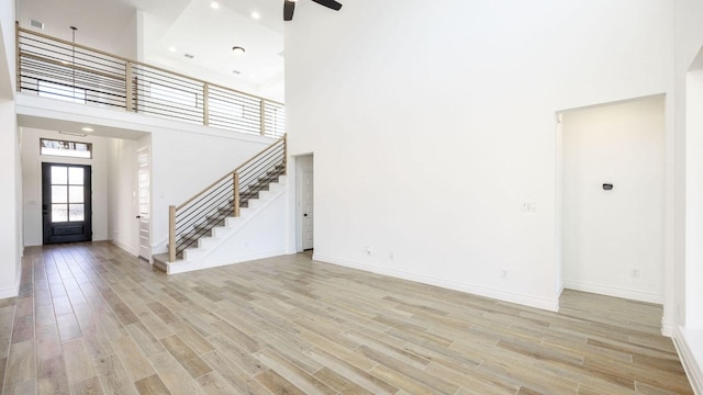 unfurnished living room featuring light wood finished floors, a high ceiling, and stairway