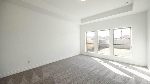 carpeted spare room with a tray ceiling and baseboards