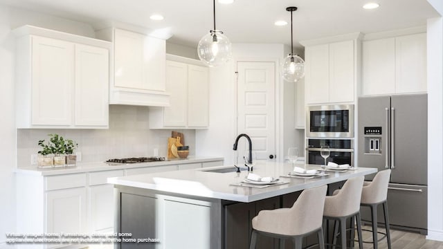 kitchen with appliances with stainless steel finishes, white cabinetry, a sink, and a center island with sink