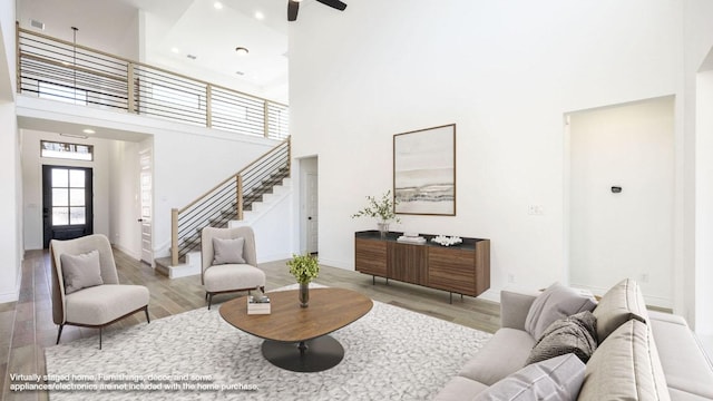 living area with a high ceiling, wood finished floors, a ceiling fan, baseboards, and stairs