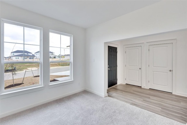 spare room featuring light wood finished floors, light colored carpet, and baseboards