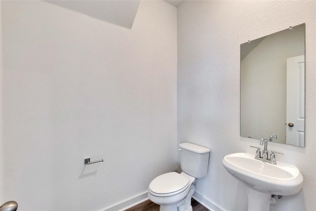 half bathroom featuring toilet, wood finished floors, baseboards, and a sink