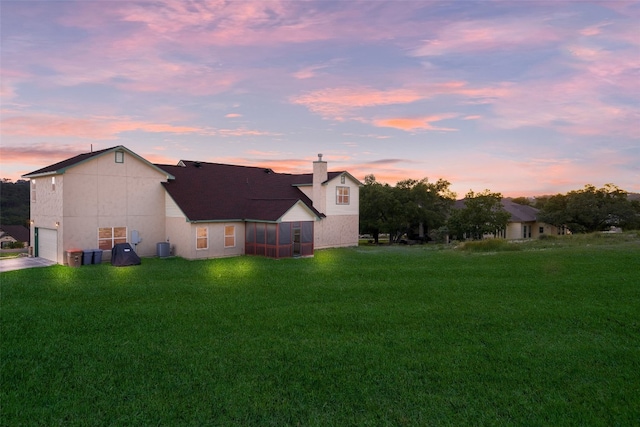 back house at dusk featuring a lawn and a garage