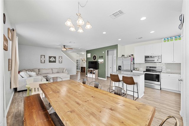 dining space with light wood-type flooring and ceiling fan with notable chandelier