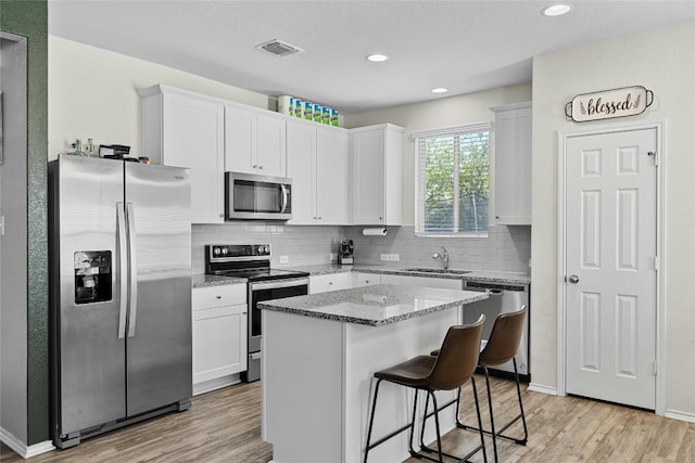 kitchen with stainless steel appliances, white cabinetry, a kitchen island, and sink