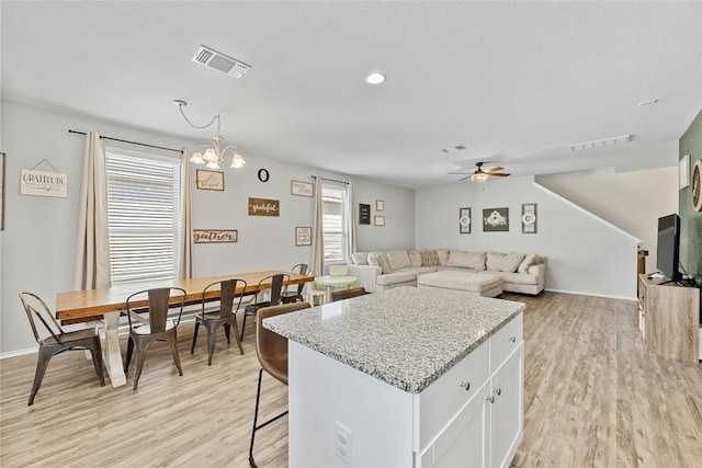 kitchen with decorative light fixtures, a kitchen breakfast bar, white cabinets, ceiling fan with notable chandelier, and light hardwood / wood-style flooring