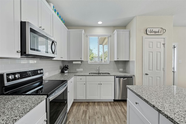 kitchen featuring white cabinetry, appliances with stainless steel finishes, tasteful backsplash, light stone counters, and sink