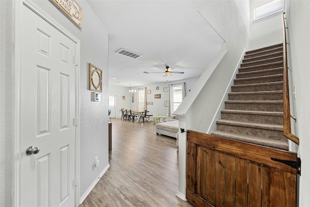 stairs featuring ceiling fan with notable chandelier and hardwood / wood-style flooring