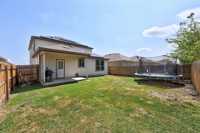 back of property featuring a patio area, a yard, and a trampoline