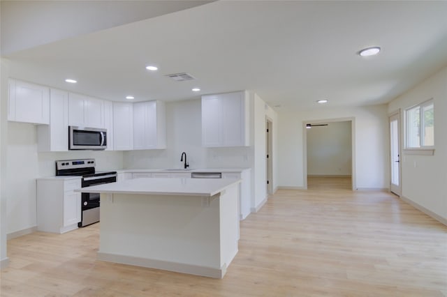 kitchen featuring a center island, sink, white cabinets, light hardwood / wood-style flooring, and appliances with stainless steel finishes