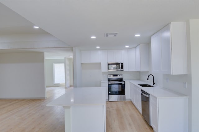 kitchen with white cabinets, stainless steel appliances, light hardwood / wood-style floors, and a center island