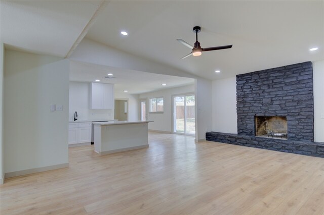 unfurnished living room with ceiling fan, lofted ceiling, sink, a stone fireplace, and light hardwood / wood-style floors