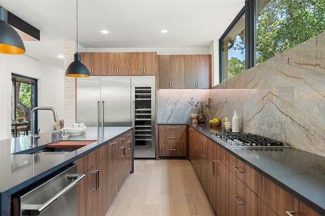 kitchen with sink, hanging light fixtures, decorative backsplash, appliances with stainless steel finishes, and light wood-type flooring