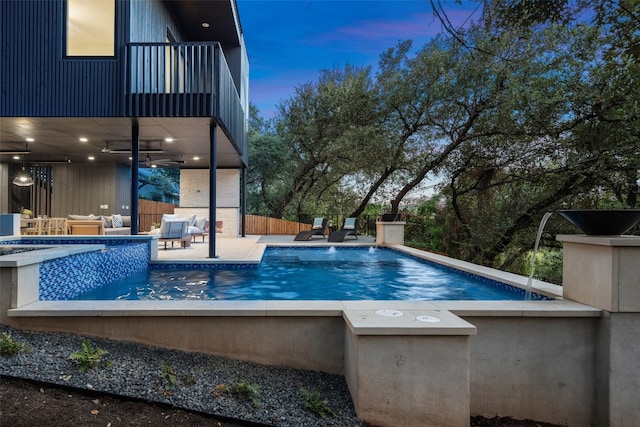 pool at dusk featuring an outdoor living space, ceiling fan, and a patio area